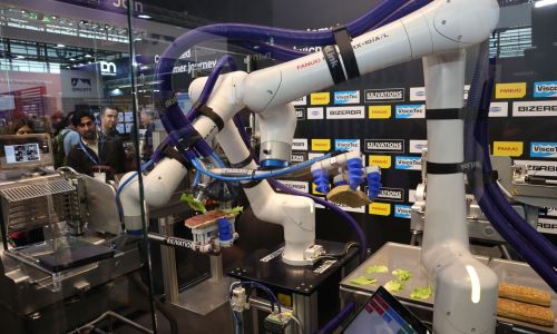 Auf einem Messestand produzieren zwei Roboterarme ein Sandwich.