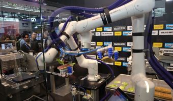 Auf einem Messestand produzieren zwei Roboterarme ein Sandwich.
