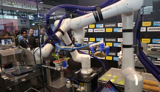 Auf einem Messestand produzieren zwei Roboterarme ein Sandwich.